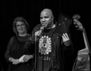 D'Vonne Lewis accepting award with Rochelle House in the background,