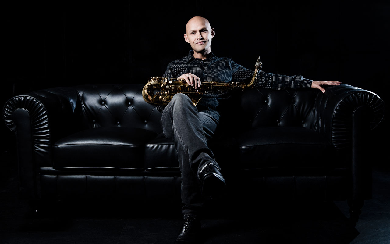 Miguel Zenon sitting on black couch holding a saxophone