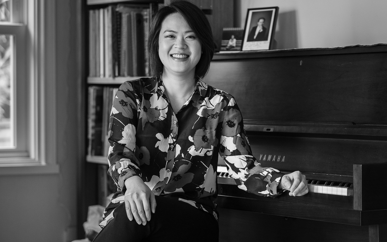 X_Julia-Tai_023_daniel-sheehan Julia Tai smiling and sitting in front of a piano.