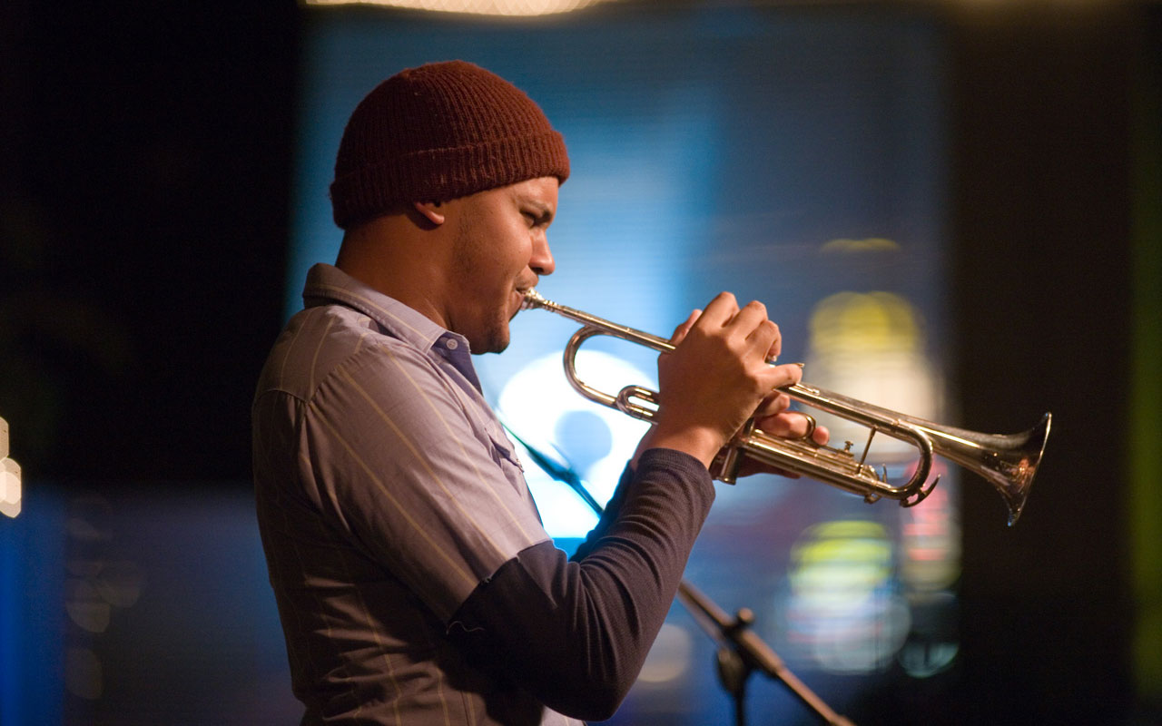 Ahamefule Oluo in profile wearing a brown beanie playing the trumpet.