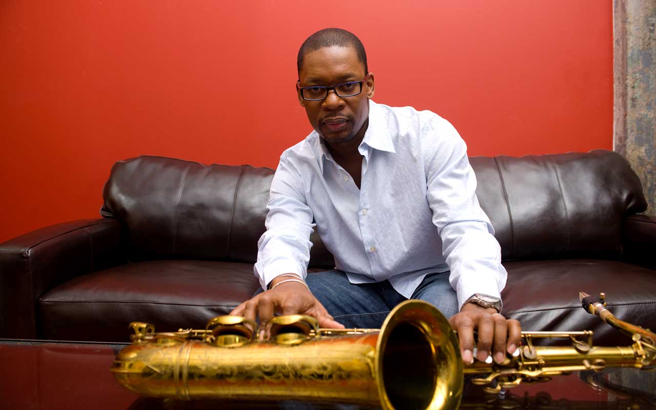 Ravi Coltrane sitting on a couch with a saxophone resting on a table in front of him.