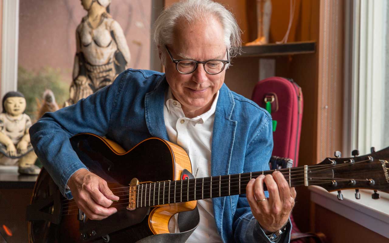 Bill Frisell by Daniel Sheehan Bill Frisell sitting in a living room playing a guitar