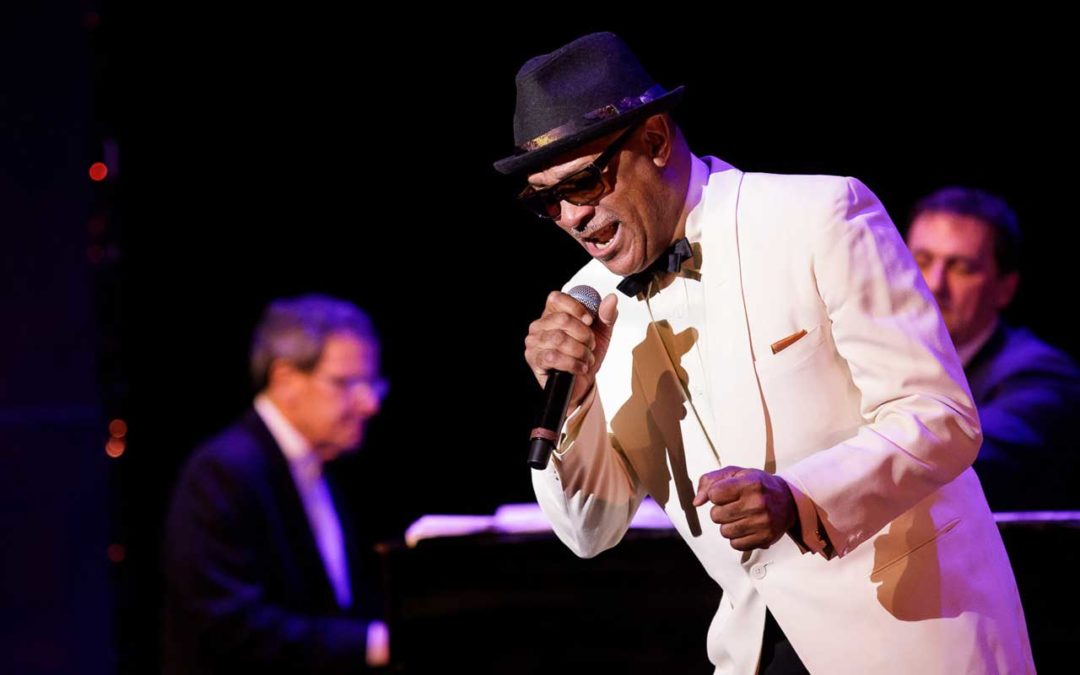 Reggie Goings singing on stage in a white tuxedo