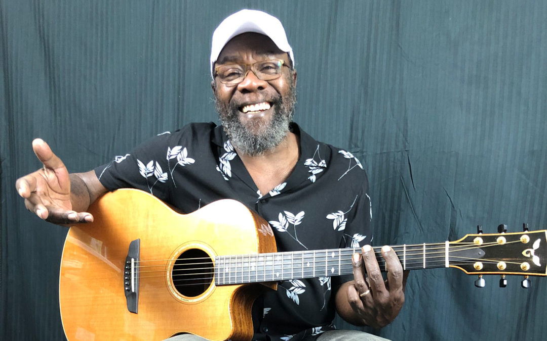 Clinton Fearon smiling playing a guitar.