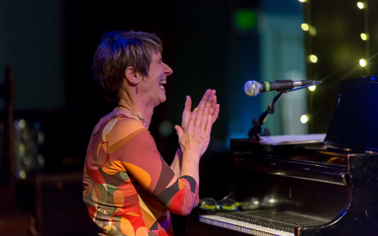 Ann Reynolds smiling and clapping at the piano.