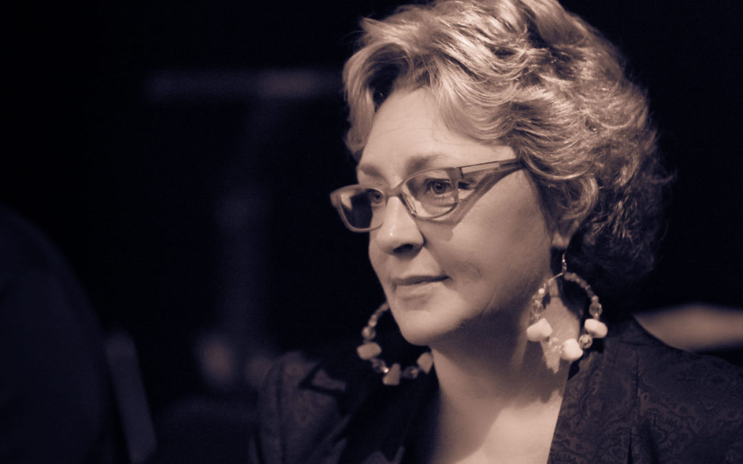 Greta Matassa wearing glasses and large round earrings, looking to the side at an angled profile.