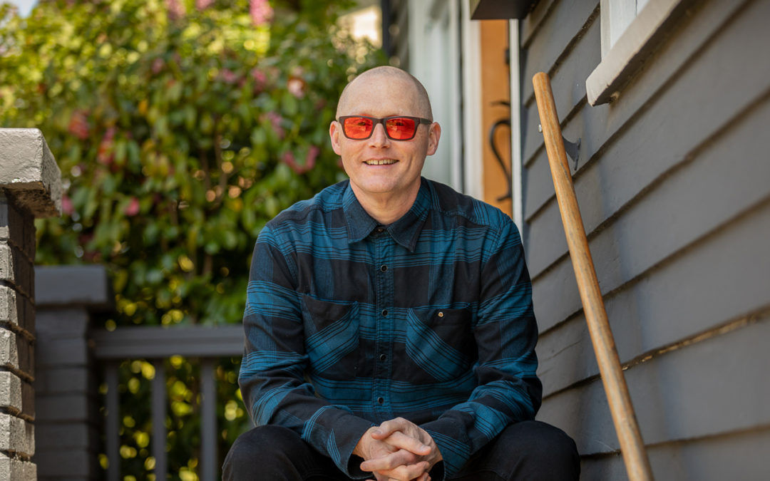 Thomas Marriott wearing orange tinted sunglasses sitting on a step.