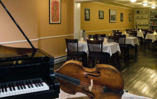 Partial view of a piano and a bass, with restaurant chairs and tables in the background