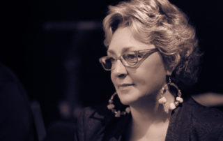 Greta Matassa wearing glasses and large round earrings, looking to the side at an angled profile.