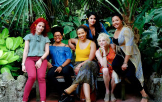 Jane Bunnett and the Maqueque band members standing in front of lush foliage.